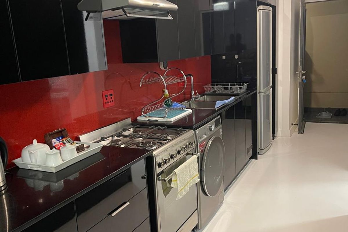 Modern kitchen featuring high-gloss black cabinetry, striking red glass splashback, black stone countertops, and integrated stainless steel appliances.