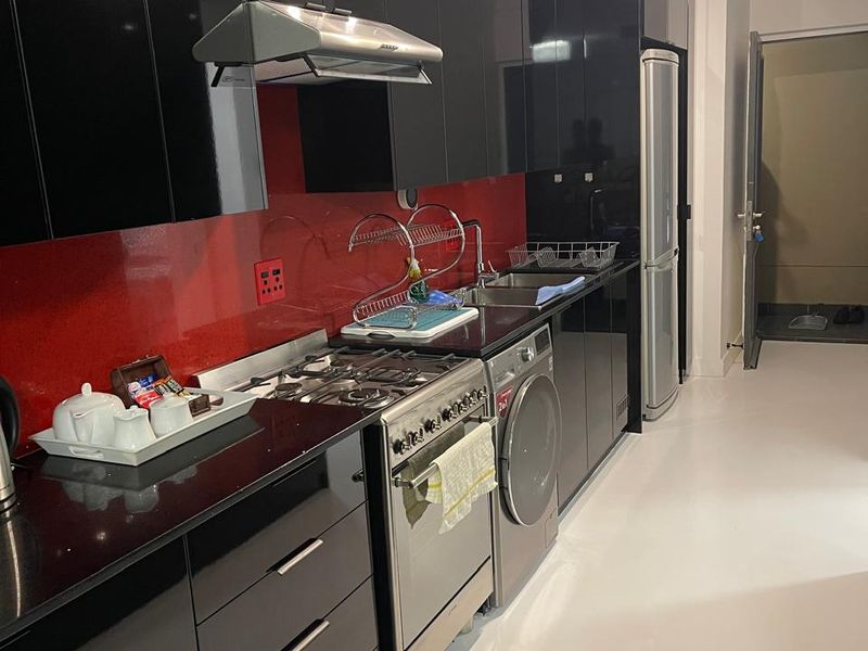 Modern kitchen featuring high-gloss black cabinetry, striking red glass splashback, black stone countertops, and integrated stainless steel appliances.