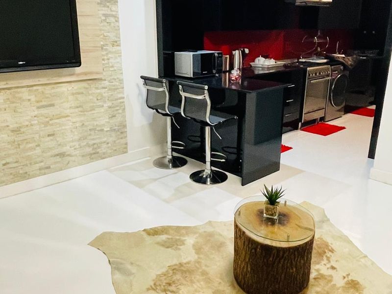Modern open-plan living area featuring a sleek black kitchen with breakfast bar, stainless steel appliances, and a decorative stone feature wall.