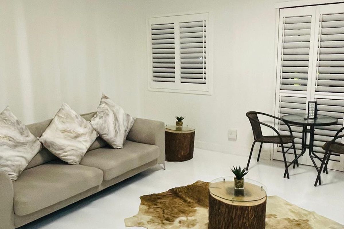 A bright living room featuring white tiled flooring, plantation shutters on the windows and doors, and a modern flush mount ceiling light fixture.