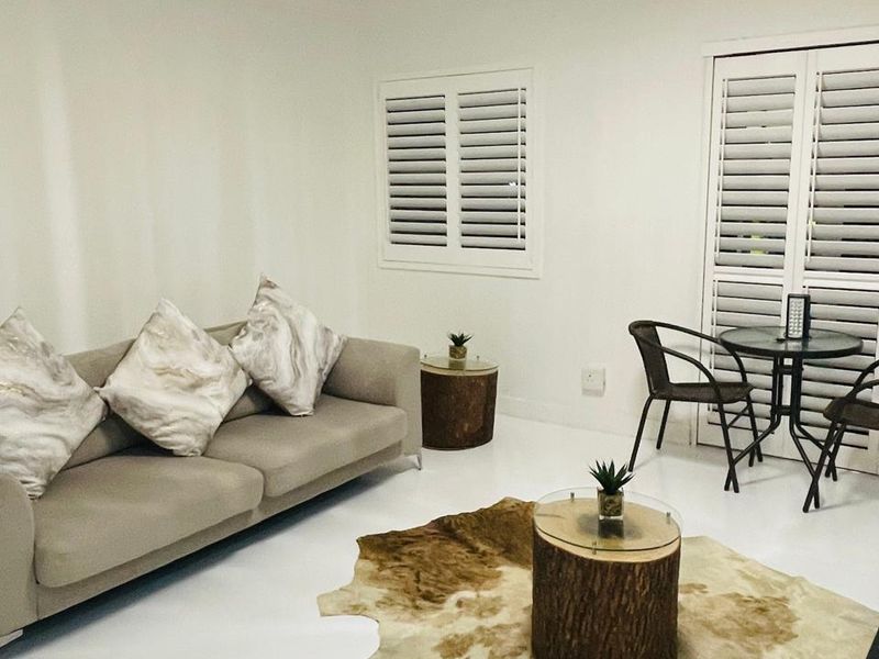 A bright living room featuring white tiled flooring, plantation shutters on the windows and doors, and a modern flush mount ceiling light fixture.