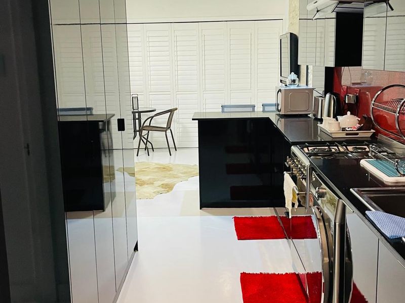 Modern kitchen featuring high-gloss black cabinetry, integrated appliances, gas hob, and sleek finishes, leading into a bright dining area with shutter blinds.