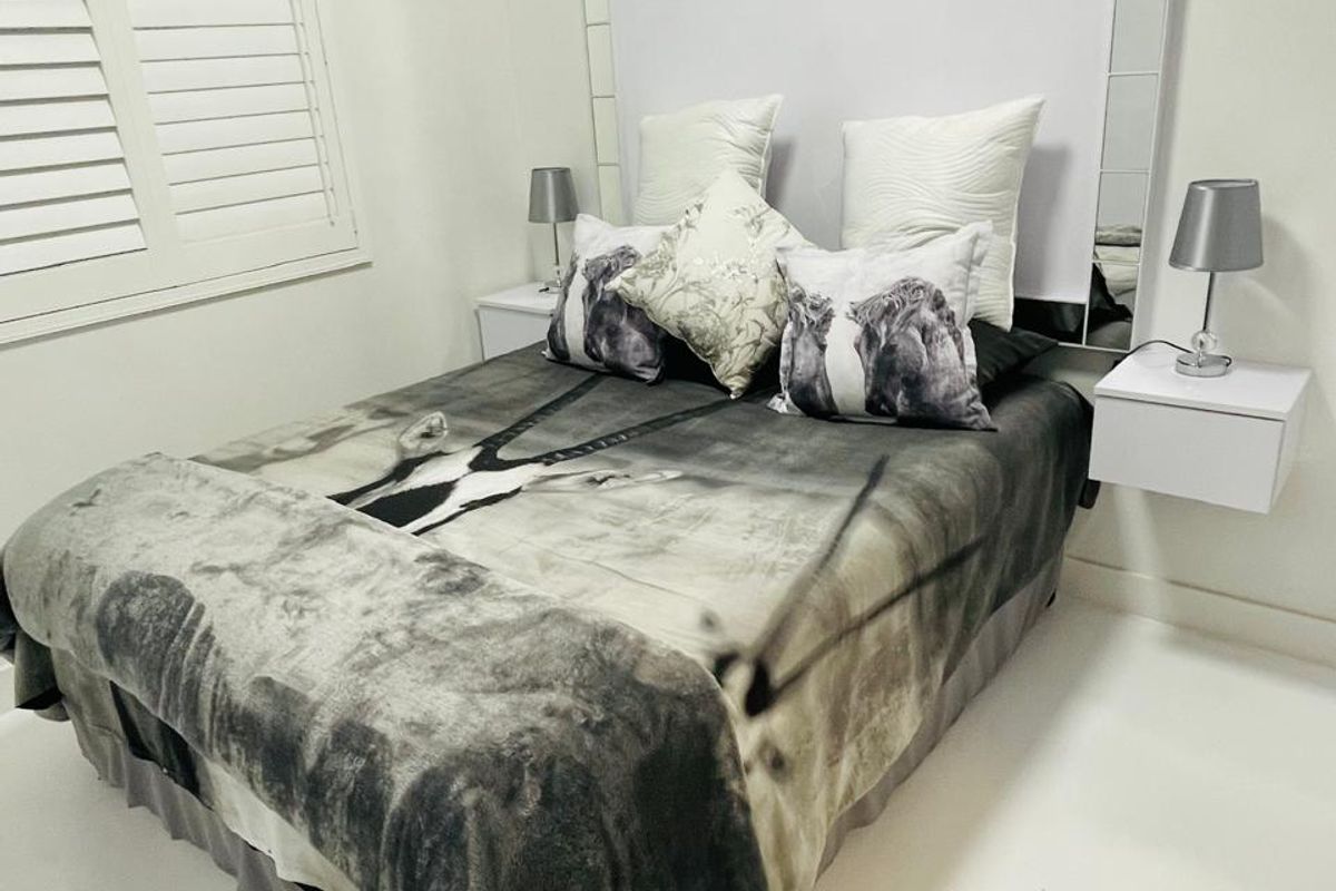 A well-maintained bedroom featuring plantation shutters, a decorative mirrored headboard panel, and modern floating bedside tables.
