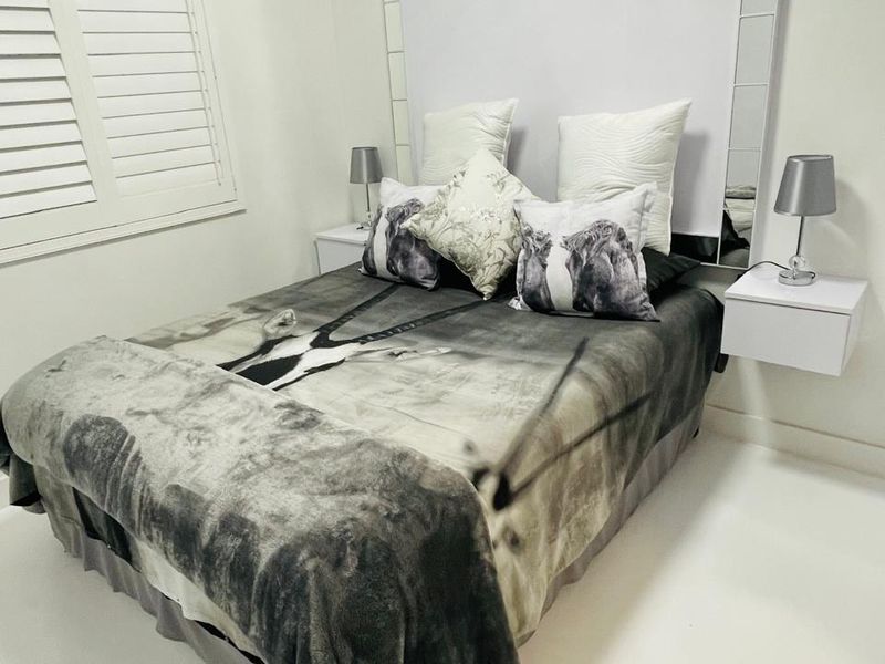 A well-maintained bedroom featuring plantation shutters, a decorative mirrored headboard panel, and modern floating bedside tables.