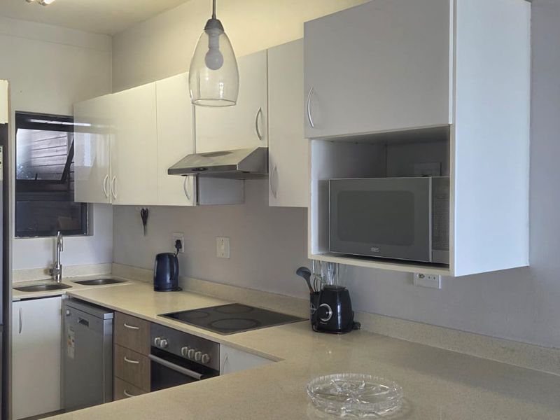 A functional kitchen featuring white cabinetry, stone countertops, integrated appliances, and a breakfast bar, with a modern pendant light fixture.