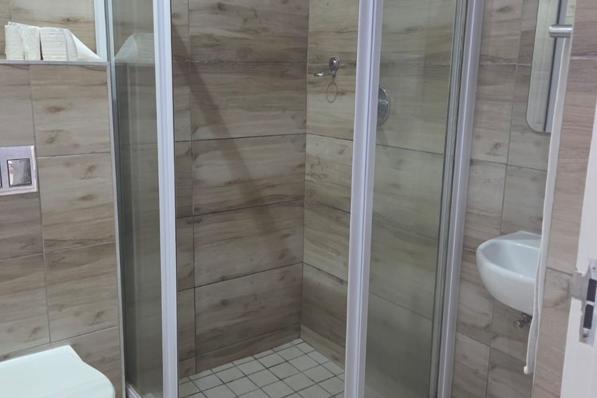 Modern bathroom featuring a glass shower enclosure, wall-mounted toilet with concealed cistern, and a compact wall-mounted basin with neutral wood-look wall tiling.