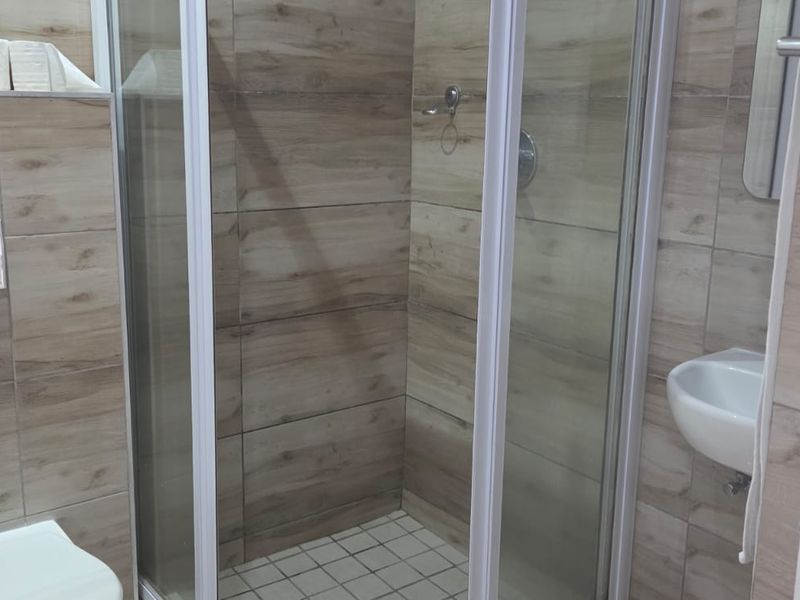Modern bathroom featuring a glass shower enclosure, wall-mounted toilet with concealed cistern, and a compact wall-mounted basin with neutral wood-look wall tiling.