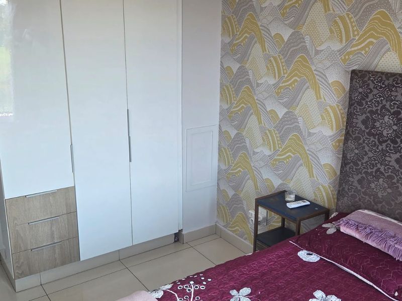 A bedroom featuring a built-in wardrobe with a mix of white and wood-grain finishes, tiled flooring, and patterned wallpaper.