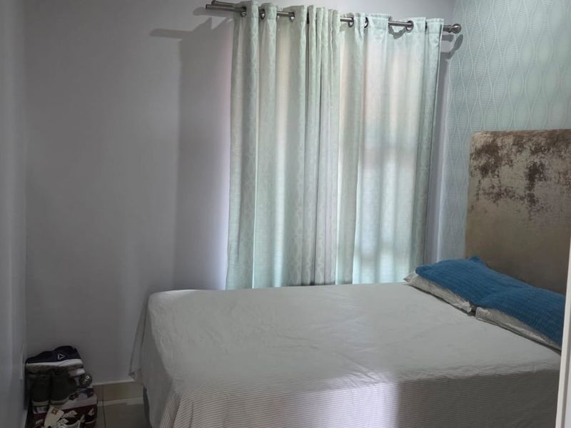 A compact bedroom featuring neutral wall finishes, textured accent wallpaper, and a window dressed with light-filtering curtains.