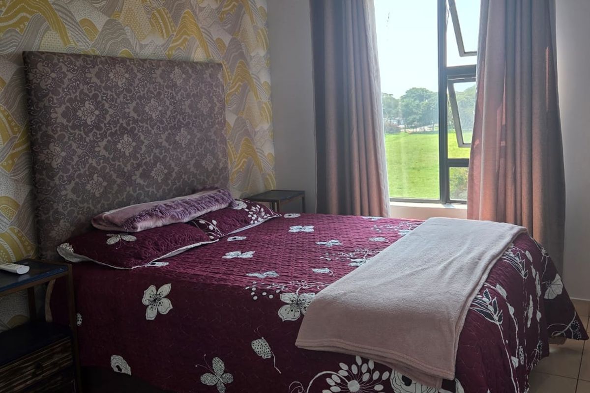 A well-lit bedroom featuring tiled flooring, a large aluminium-framed window with natural views, and a decorative feature wall.