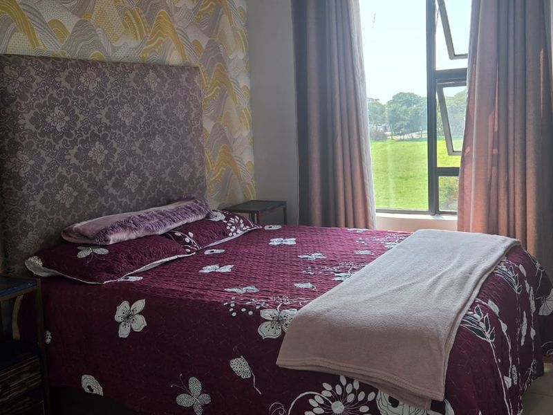 A well-lit bedroom featuring tiled flooring, a large aluminium-framed window with natural views, and a decorative feature wall.