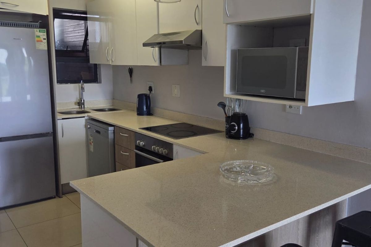 Modern kitchen featuring sleek white cabinetry, stone countertops, integrated appliances, and a breakfast bar, seamlessly connected to an outdoor balcony area.