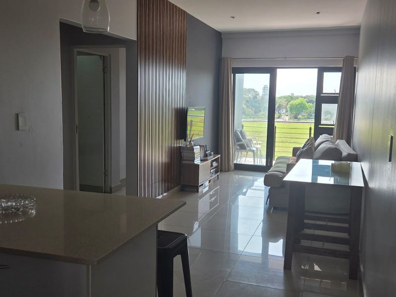 Open-plan living area featuring tiled floors, a modern kitchen counter, and a feature wall, leading out to a balcony with natural light.