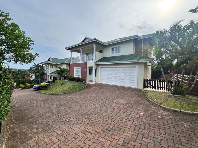 Front exterior view of a two-story townhouse featuring a paved driveway, double garage, and an upper-level balcony with a tiled roof.