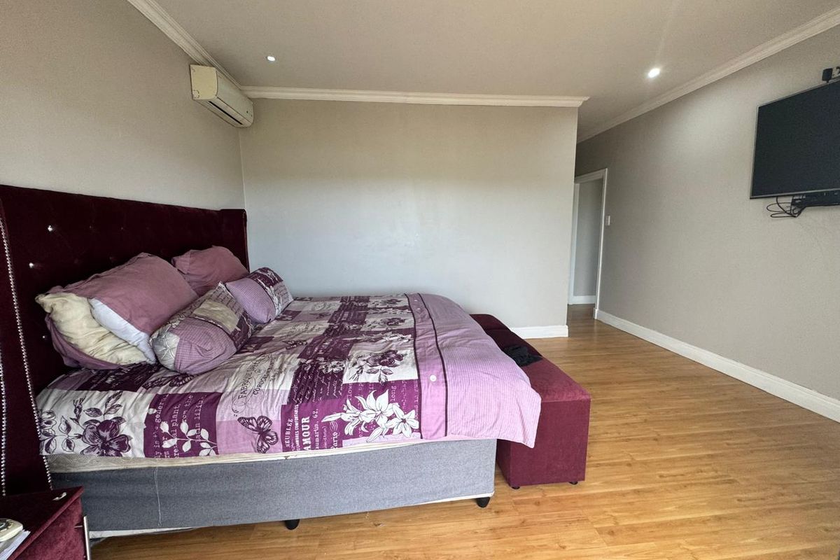 Spacious bedroom featuring laminate flooring, recessed downlighting, and a wall-mounted air conditioning unit.