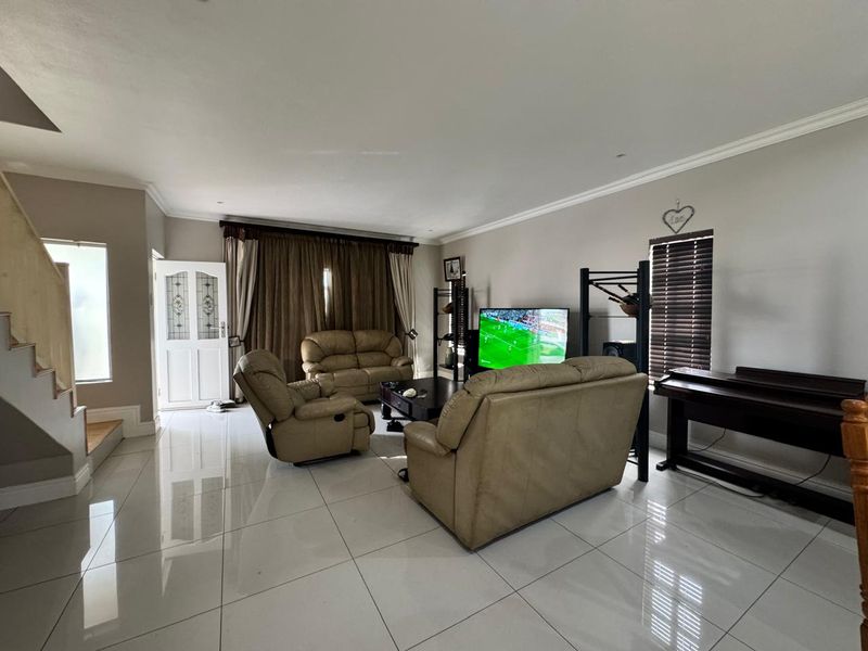 Spacious living room featuring polished floor tiles, a staircase, and natural light through a panelled front door and window with venetian blinds.