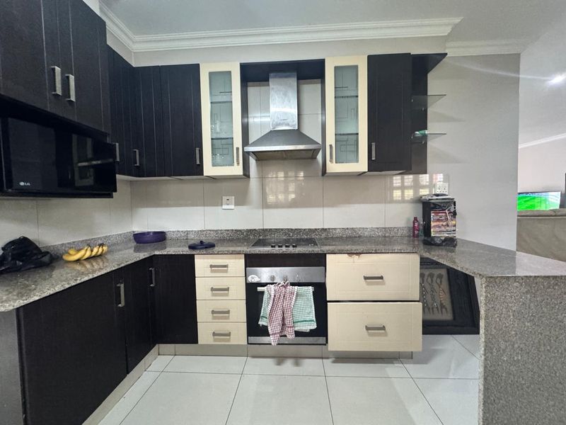 A functional kitchen featuring granite countertops, built-in cabinetry, and integrated appliances, including an oven, hob, and extractor fan.
