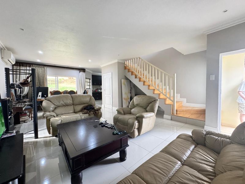 Spacious open-plan living area featuring tiled flooring, recessed lighting, and a wooden staircase leading to the upper level.