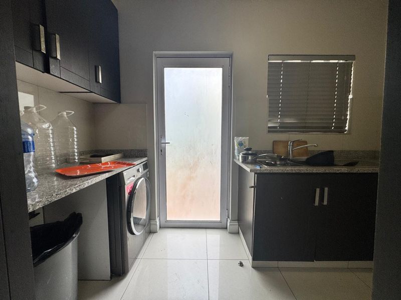 A functional laundry room featuring dark cabinetry, granite countertops, a stainless steel sink, and direct access to the exterior via a frosted glass door.
