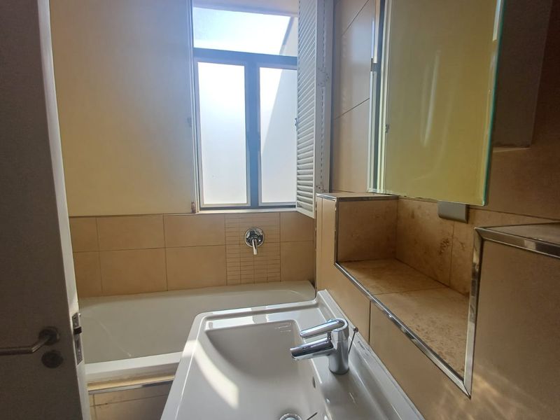 A functional bathroom featuring a bathtub, basin with mixer tap, tiled walls, and a built-in vanity shelf with a mirror.