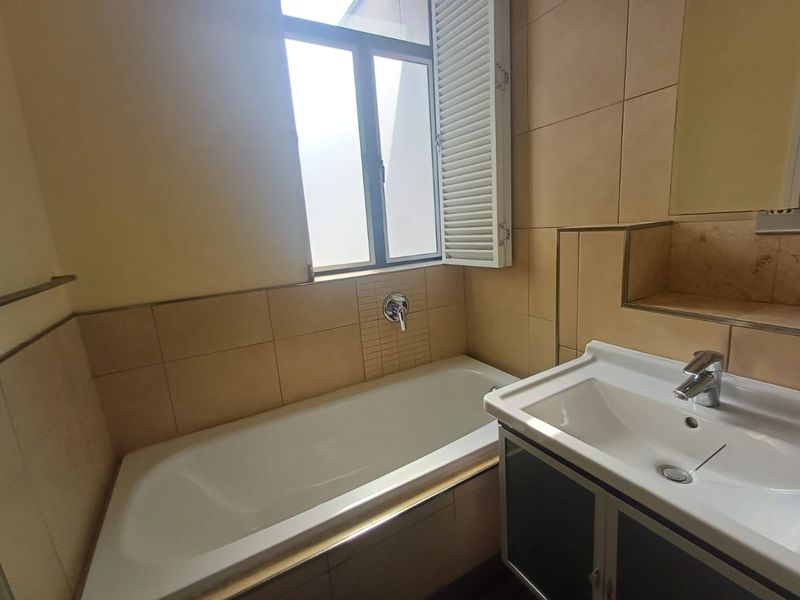 A functional bathroom featuring a bathtub, vanity basin, and tiled walls, complemented by window shutters for privacy and natural light.