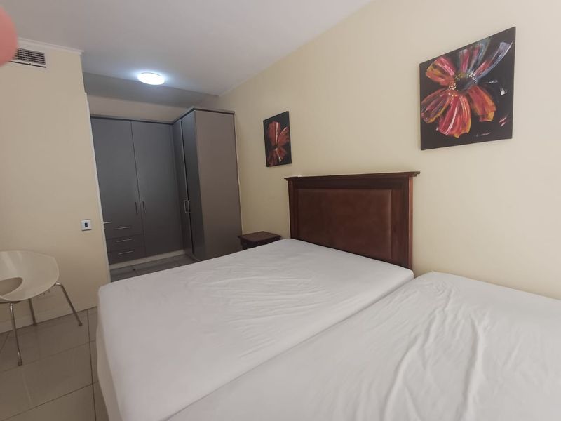 A functional bedroom featuring built-in cupboards, tiled flooring, and neutral wall finishes, providing a clean and practical living space.