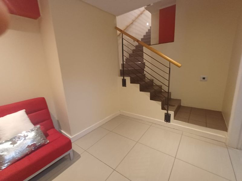 A bright hallway featuring a modern staircase with a metal balustrade, wooden handrail, and neutral tiled flooring.