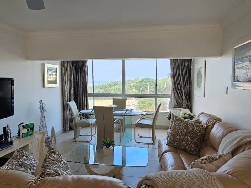 Open-plan living and dining area featuring large windows with natural light, tiled flooring, and a ceiling fan, offering a comfortable and functional living space.