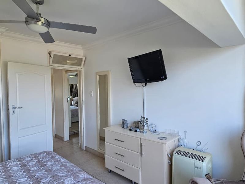 A functional bedroom featuring tiled flooring, a ceiling fan, and a built-in wardrobe with mirrored sliding doors.