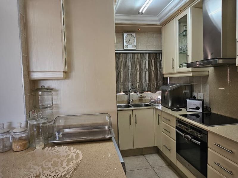 A functional kitchen featuring built-in cabinetry, stone countertops, a stainless steel extractor fan, and integrated oven and hob, with tiled flooring throughout.