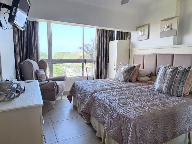 A well-lit bedroom featuring large floor-to-ceiling windows with scenic views, tiled flooring, and a built-in headboard.