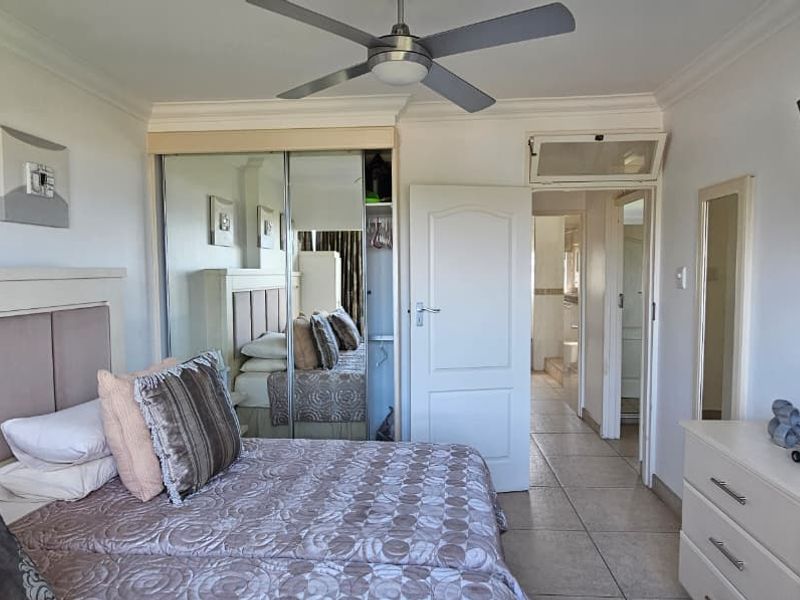 A bedroom featuring tiled flooring, a ceiling fan, and a built-in mirrored wardrobe with access to an adjoining hallway.