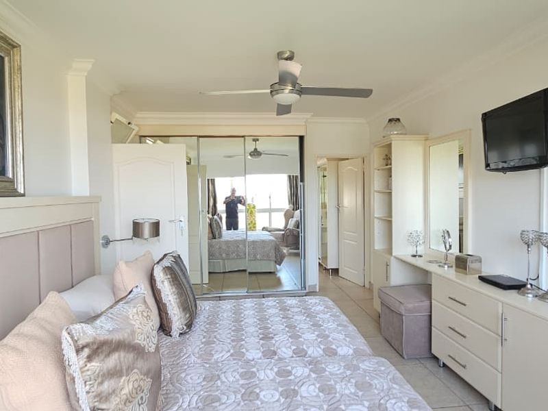 A well-maintained bedroom featuring tiled flooring, a ceiling fan, and built-in mirrored wardrobes with an integrated vanity area.