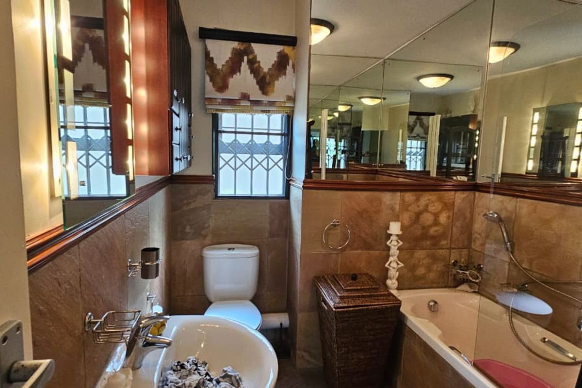 A functional bathroom featuring tiled walls, a built-in vanity, a bathtub with shower mixer, and a toilet, with large wall-mounted mirrors.