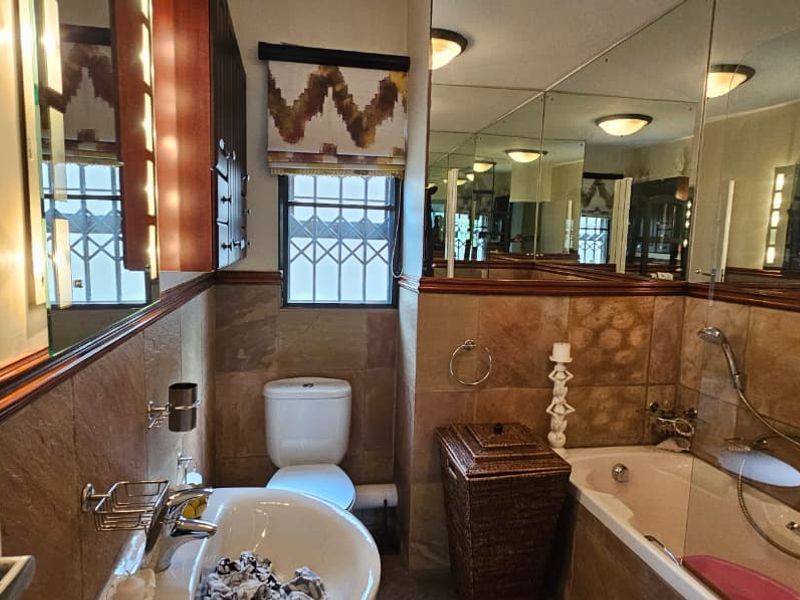 A functional bathroom featuring tiled walls, a built-in vanity, a bathtub with shower mixer, and a toilet, with large wall-mounted mirrors.