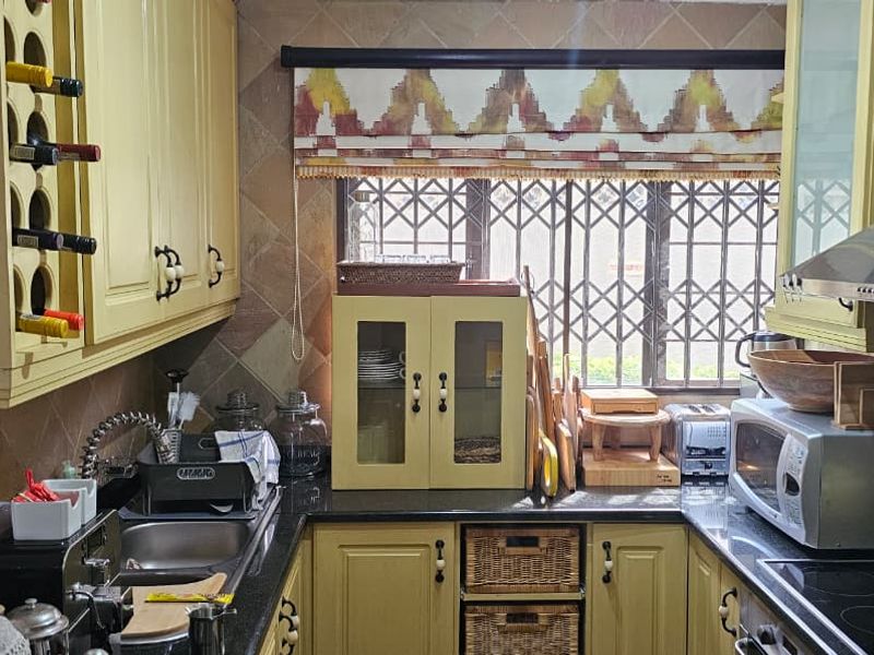 A compact kitchen featuring yellow cabinetry, granite countertops, integrated appliances, and a window with security bars.