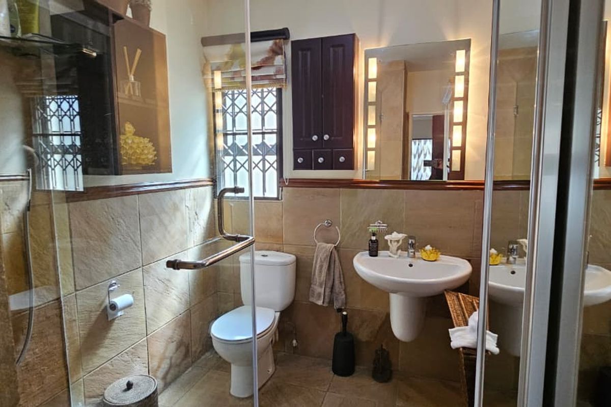 A functional bathroom featuring a pedestal washbasin, toilet, and a glass-enclosed shower with tiled finishes and wall-mounted storage cabinetry.