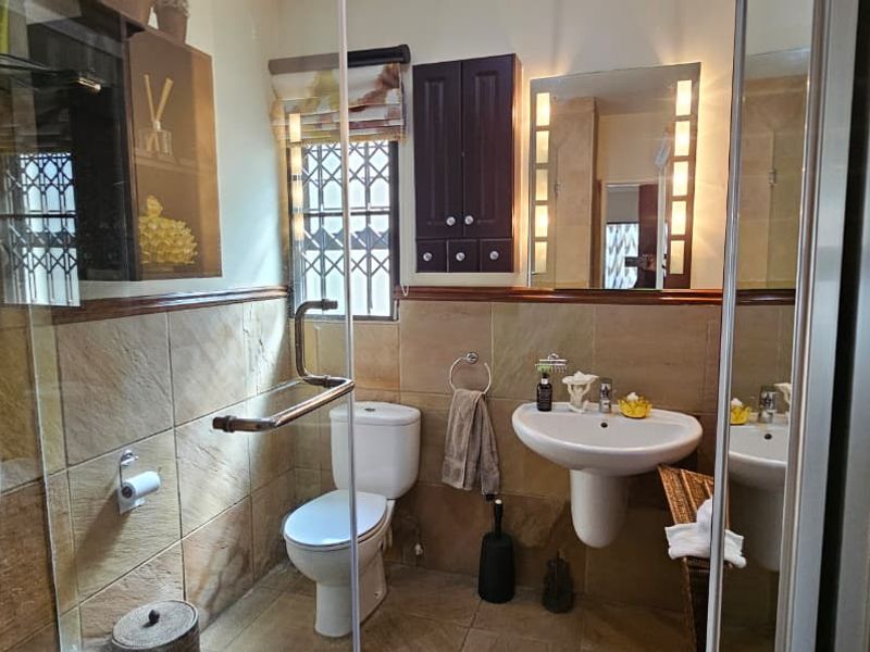 A functional bathroom featuring a pedestal washbasin, toilet, and a glass-enclosed shower with tiled finishes and wall-mounted storage cabinetry.