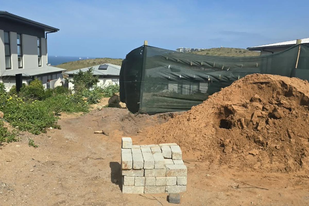 A view of a vacant residential plot showing site preparation, exposed soil, and temporary construction fencing in a developed neighborhood.