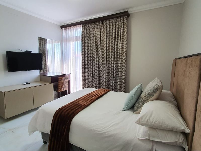 A well-maintained bedroom featuring tiled flooring, neutral wall finishes, and a sliding glass door with floor-to-ceiling curtains providing natural light.