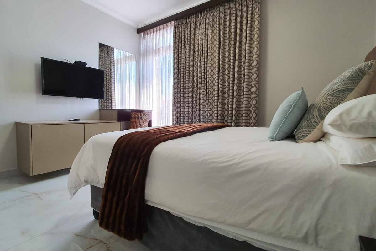 A well-maintained bedroom featuring marble flooring, a built-in vanity unit, and large sliding glass doors with floor-to-ceiling curtains.