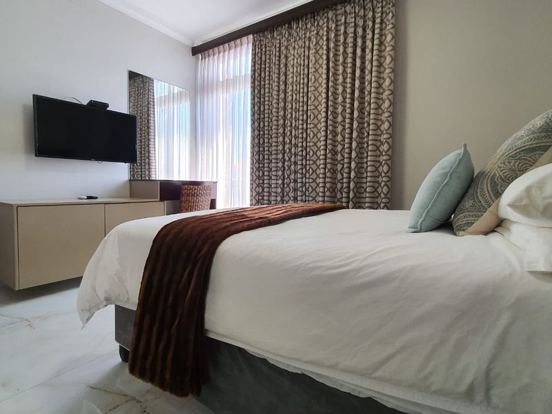 A well-maintained bedroom featuring marble flooring, a built-in vanity unit, and large sliding glass doors with floor-to-ceiling curtains.