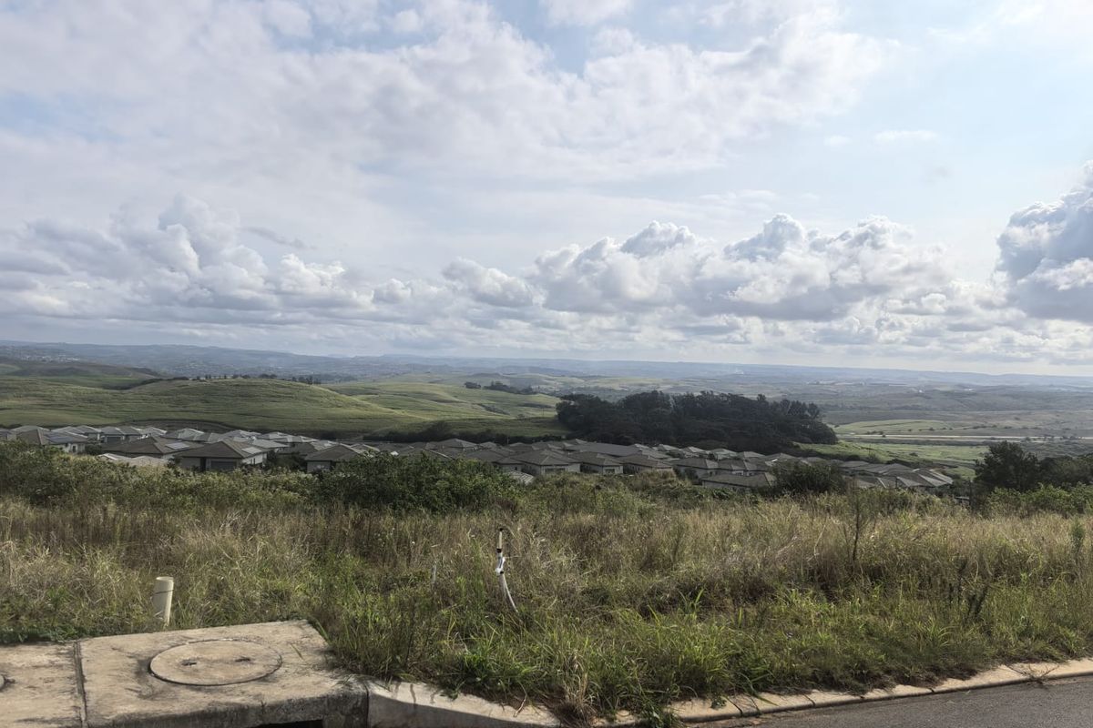 Elevated view overlooking a residential estate and surrounding rolling hills, featuring a foreground stormwater drain and natural vegetation.