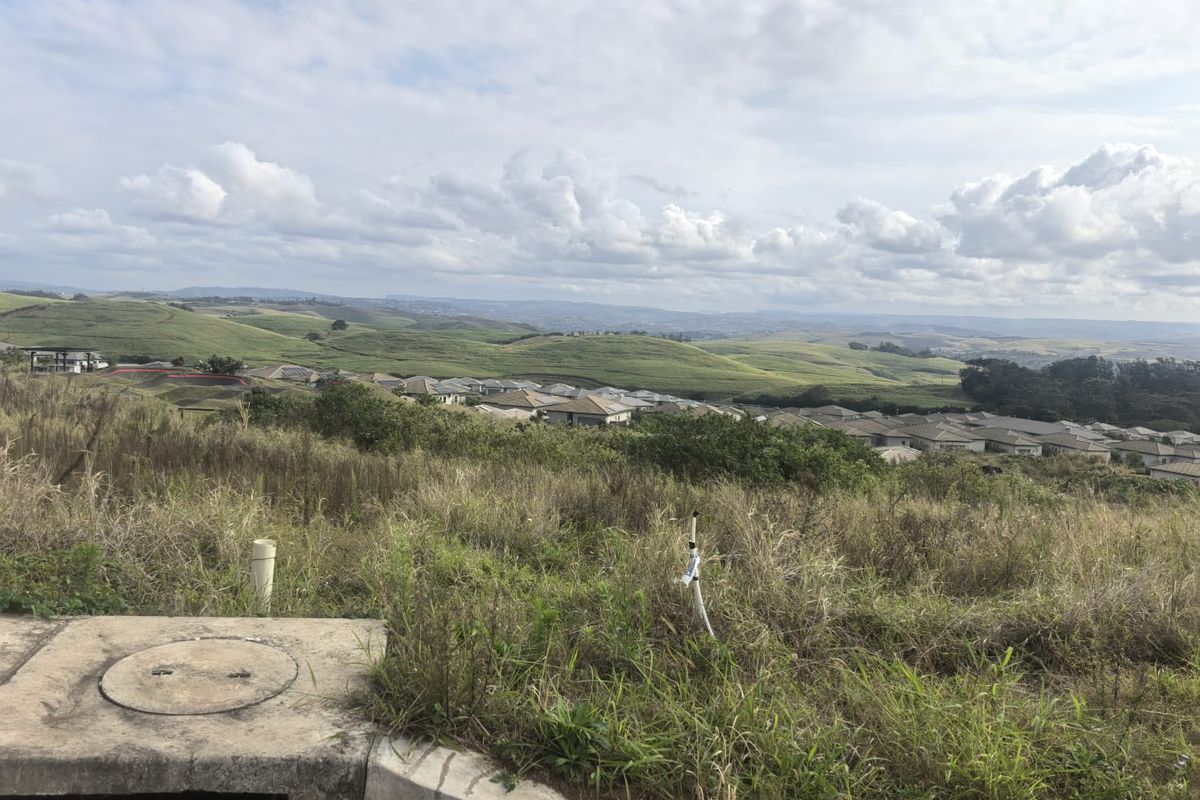 Elevated view overlooking a residential estate and surrounding rolling green hills, showcasing the landscape potential of the vacant land.