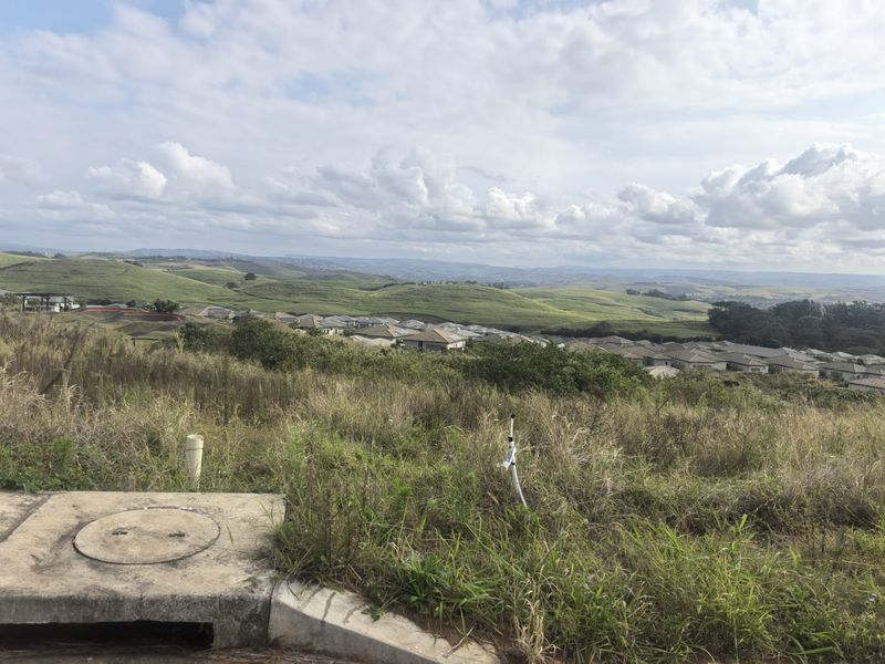 Elevated view overlooking a residential estate and surrounding rolling green hills, showcasing the landscape potential of the vacant land.