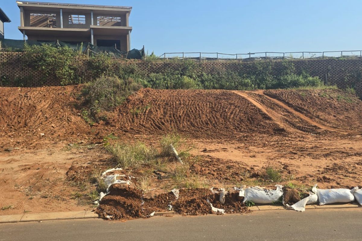 A vacant residential plot featuring an elevated slope, retaining wall structure, and direct street access, ready for development.