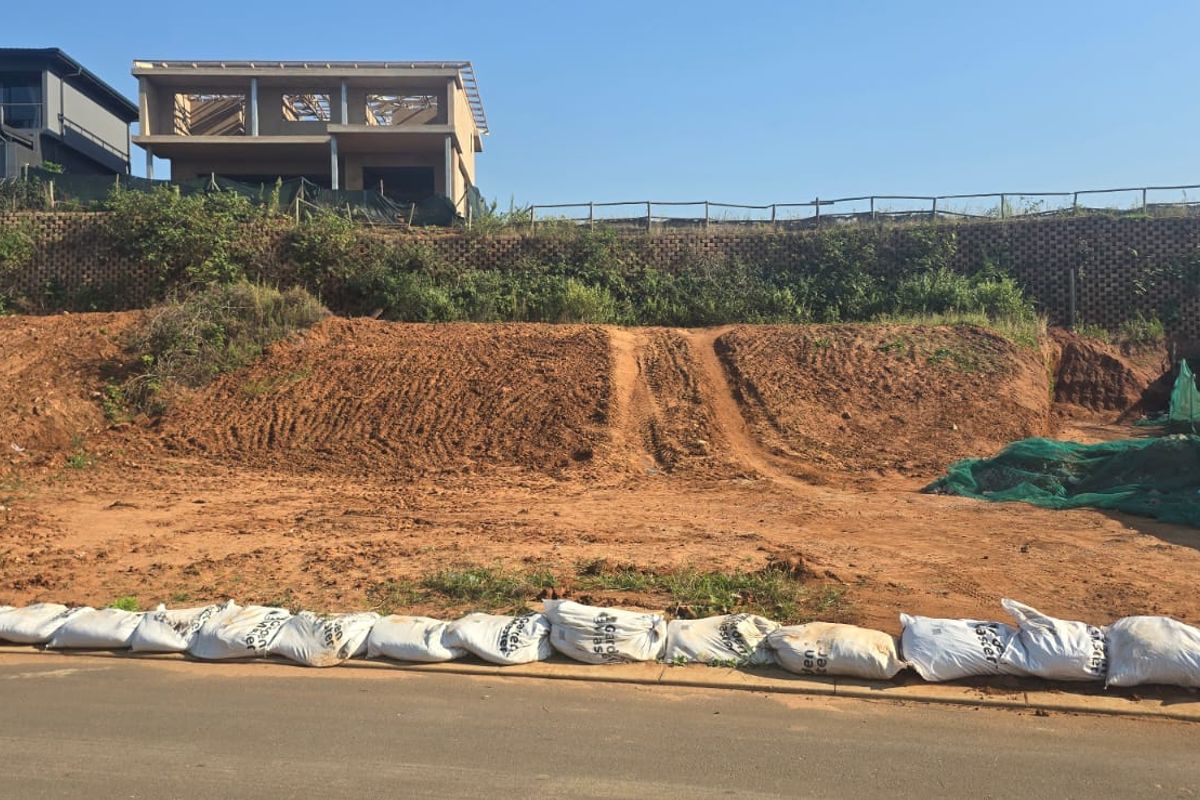 Vacant residential land plot featuring a sloped terrain and a retaining wall, situated in a developing neighborhood.