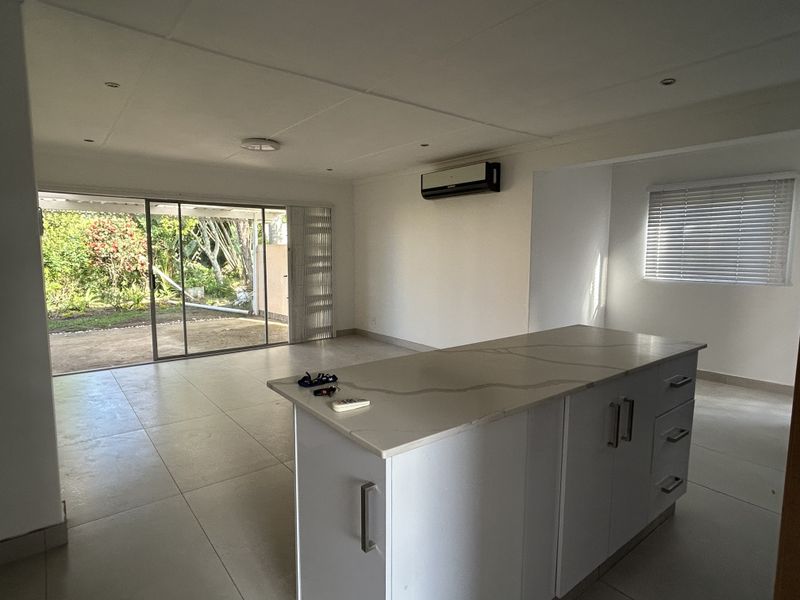 Spacious open-plan living area featuring a modern kitchen island, tiled flooring, split-system air conditioning, and large sliding doors opening to a private garden.