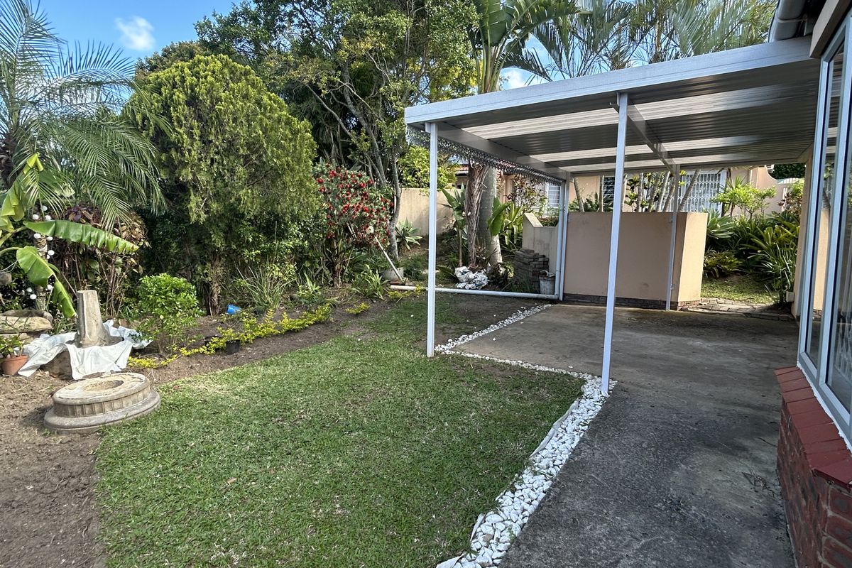 Rear garden area featuring a metal carport, concrete driveway, and established landscaping with a brick retaining wall.