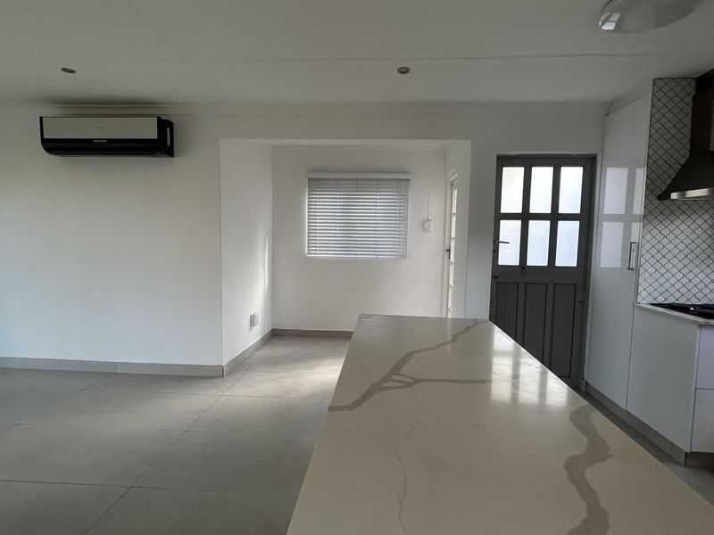 Modern open-plan living area featuring a kitchen island with stone countertops, tiled flooring, and a wall-mounted air conditioning unit.